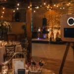 Holz-Fotobox mit Sofortdrucker in einer stilvollen Hochzeitslocation mit festlich gedeckten Tischen, Tanzfläche und stimmungsvoller Beleuchtung.