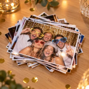 Stapel frisch gedruckter Fotobox-Bilder auf einem Holztisch, obenauf ein Gruppenfoto lachender Gäste mit Papierbrillen und Hüten